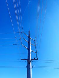 Low angle view of electricity pylon against clear blue sky