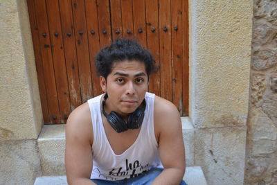 Portrait of young man sitting against wall