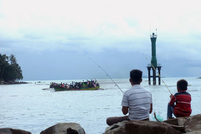 Rear view of people fishing in sea against sky