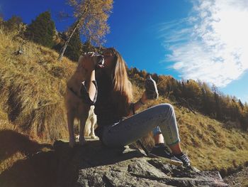 Young woman kissing golden retriever while sitting on rock against sky