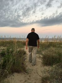 Rear view full length of man walking at beach against sky during sunset