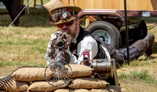 Full length portrait of man aiming gun while lying on field