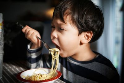 Close-up of boy eating pasta in bowl at table