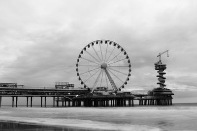 Ferris wheel in sea against cloudy sky