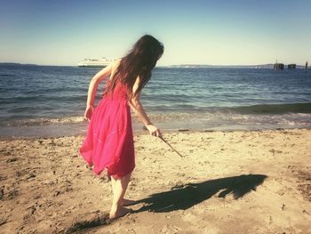 Girl holding stick at beach against clear sky on sunny day