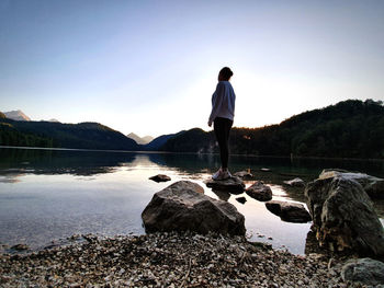 Rear view of man standing on rock by lake against sky