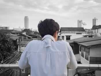 Rear view of man looking at city buildings against sky