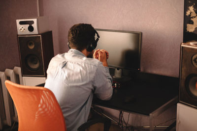 Concentrated man in headphones sitting by desktop computer