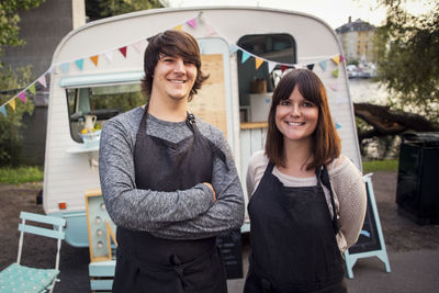 Portrait of happy owners standing on street against food truck