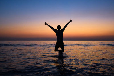 Silhouette man standing in sea against sky during sunset