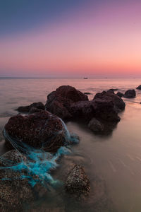 Rocks on beach against sky during sunset