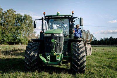 Farmer standing on tractor at field under sky