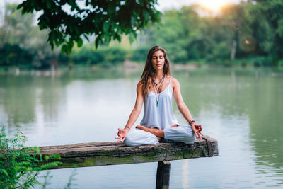 Woman doing yoga while sitting on pier at lake