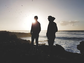 Silhouette people on beach against sky during sunset