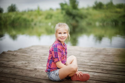 Portrait of girl sitting on wood by lake