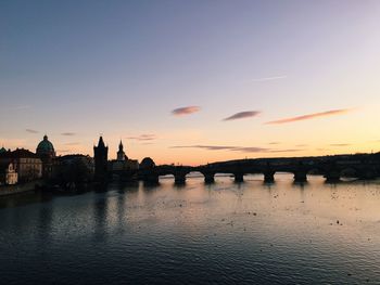 Charles bridge over vltava river against sky during sunset