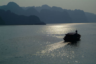 Silhouette boat in sea against mountains