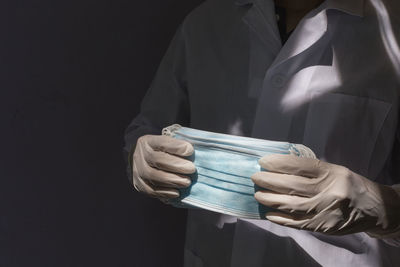 Cropped image of man holding protective face mask against black background