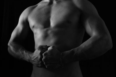 Midsection of shirtless muscular man standing against black background