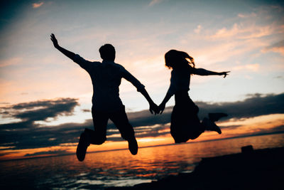 Silhouette men jumping against sky during sunset