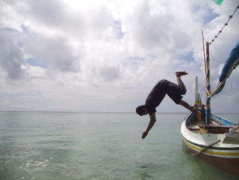 Man diving into sea against cloudy sky