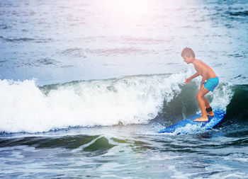 Full length of shirtless man surfing in sea