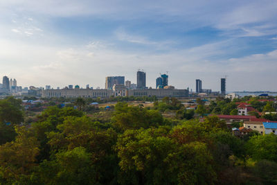 Trees and buildings in city against sky