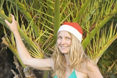 Portrait of young woman wearing santa hat while standing by tree