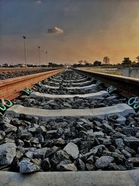 Surface level of railroad track against sky during sunset