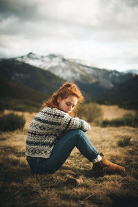 Woman sitting on field against mountains
