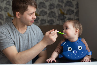 Young father feeding his baby in the kitchen. family time and gender equality concept. lifestyle