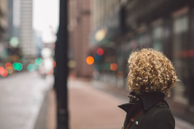 Side view of woman standing on sidewalk in city