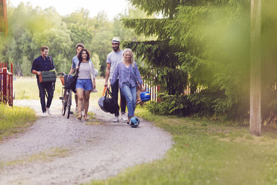 Full length of friends with luggage and bicycle walking on footpath