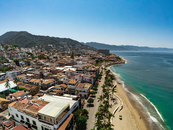 High angle view of townscape by sea against clear blue sky