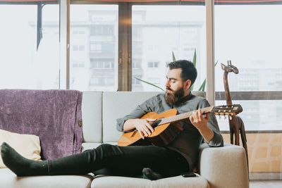 Young man playing guitar on sofa at home