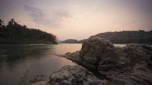 Rocks by sea against sky during sunset