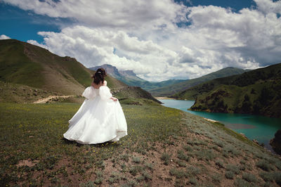 Rear view of a beautiful bride, woman running through the grass on a hill in the mountains while the