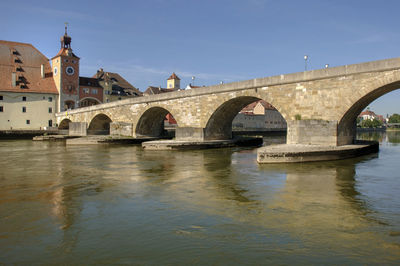 Arch bridge over river by buildings against clear sky