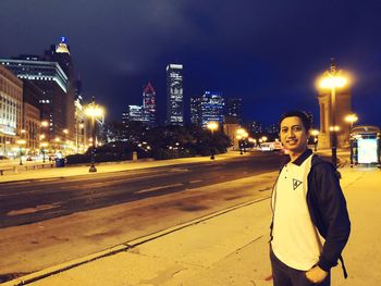 Man standing on road by illuminated buildings against sky at night