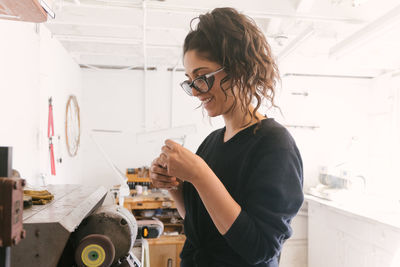 Female jeweler smiling while working at grinder at home studio space