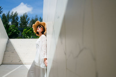 Woman looking away while standing against wall