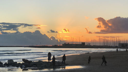 Silhouette people on beach against sky during sunset