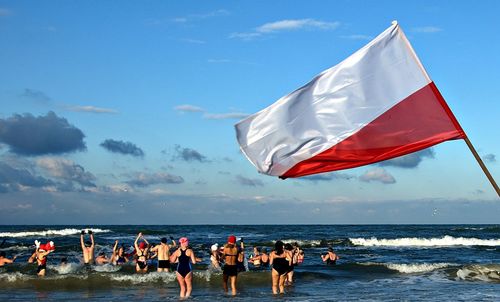 People enjoying in sea with polish flag at beach against sky