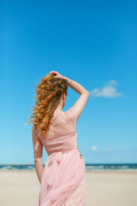 Rear view of woman standing at beach against blue sky