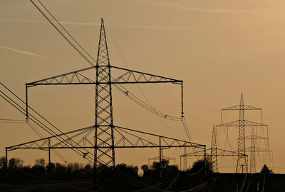 Low angle view of silhouette electricity pylon against sky during sunset