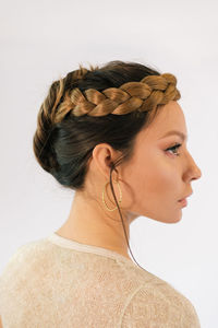 Side view of beautiful young female model with elegant braided hairstyle and makeup and with golden hoop earrings against white background