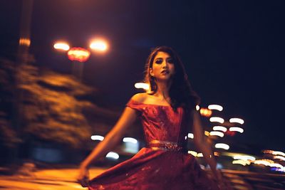 Portrait of young woman in dress standing at illuminated city