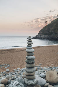 Stack of pebbles on beach against sky during sunset