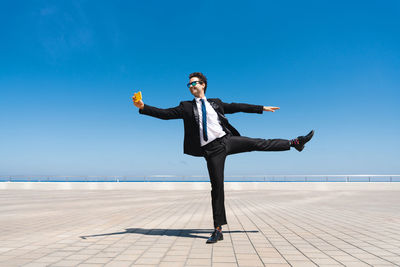 Full length of woman jumping on beach against blue sky