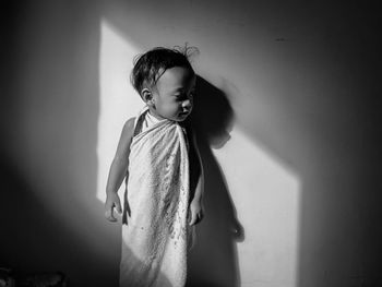 Girl looking away while standing against wall at home